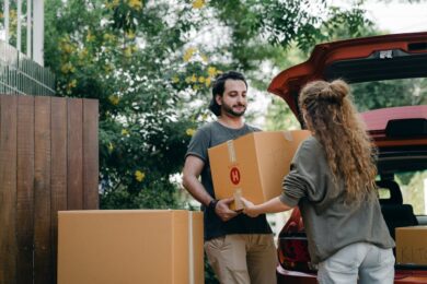Woman and man carrying cardboard boxes, red car, moving, relocation